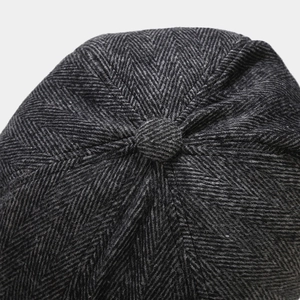 Macro shot of dark grey herringbone wool newsboy cap showing top button and fabric texture