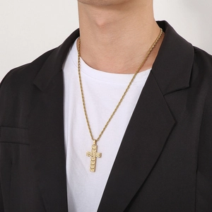 Close-up of a gold textured cross pendant on a rope chain worn with a black blazer suit
