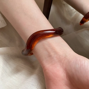 Close-up of irregular wave-shaped amber resin bangle with glossy translucent finish