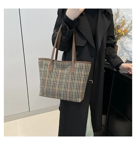 Detail of checkered tote bag showing houndstooth fabric and brown leather handle