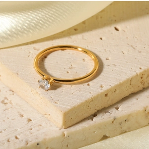 Détail d'une bague minimaliste dorée ornée d'un zircon rond sur une surface en soie et pierre