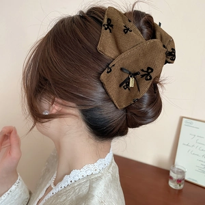 Macro detail of brown tweed bow hair claw clip with golden pendant and embroidery
