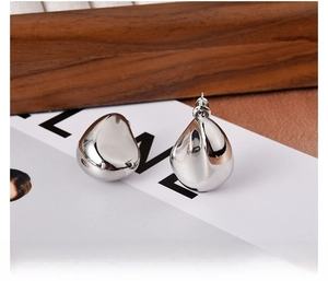 Macro view of silver teardrop stud earrings with polished metallic finish on a textured background