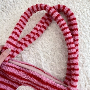 Macro detail of plush red and pink striped shoulder bag strap with curly fleece texture