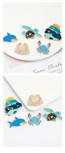Detail shot of ocean themed enamel pins featuring crab shark turtle and frog designs