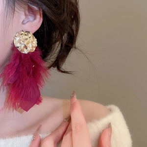 Macro detail of oversized gold textured stud earrings with vibrant magenta feathers