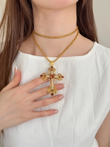 Détail d'un collier croix doré vintage avec strass ambrés porté par un mannequin