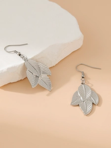 Macro view of silver leaf-shaped pendant earrings on white textured stone decor