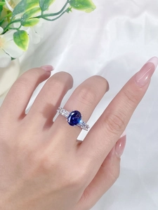 Macro shot of oval blue sapphire silver ring with accent diamonds on finger