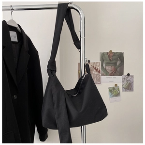 Minimalist black canvas shoulder bag with unique knotted strap detail on clothing rack