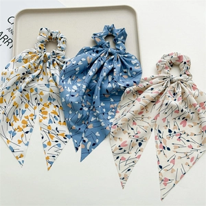 Close-up of three floral chiffon hair scrunchies with long ribbons in a soft tray