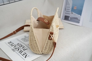 Detail view of woven straw bag with leather handles and gold metal lock on white background