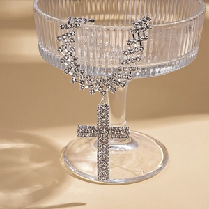 Gros plan d'un pendentif croix argenté avec zircons suspendu au bord d'un verre