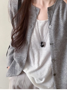 Silver bead chain necklace with black Saturn orb pendant worn on a grey knit cardigan