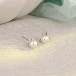 Close-up of cat-ear pearl stud earrings in silver metal on soft fabric background