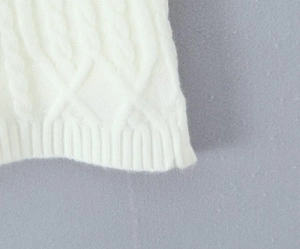 Close-up of white cable knit texture showing detailed braided patterns on a knitted sweater