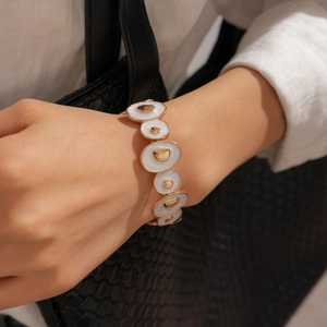 Détail d'un bracelet bohème en émail crème et or sur le poignet d'une femme