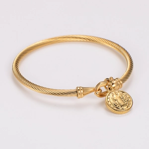 Macro detail of golden spiral cable bangle with an embossed religious saint pendant