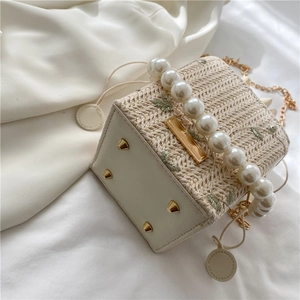 Elegant straw bucket bag with pearl handle and green leaf embroidery on silk background