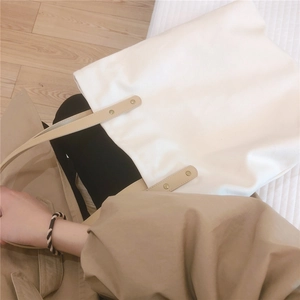 Detail view of large white canvas tote bag with beige leather handles and gold rivets