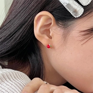 Close-up of mini red apple stud earring with green leaf detail worn on a model's ear