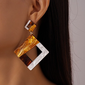 Close-up of geometric resin drop earrings in amber and white on a model's ear