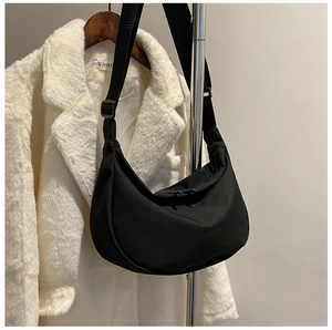 Close-up of black half-moon nylon bag featuring dual zippers and wide adjustable shoulder strap
