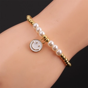 Detailed shot of gold beads and pearls bracelet with a smiley face charm on a model's wrist