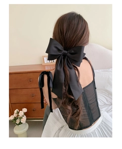 Detail of a large black satin bow hair clip worn by a model in a cozy bedroom setting