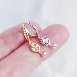 Macro shot of silver and gold key-shaped earrings with inlaid clear zircon gemstones