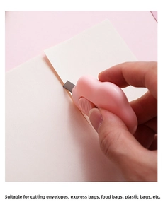 Pink cloud-shaped utility knife cutting through paper with its retractable metal blade