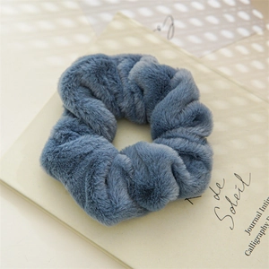Close-up of a soft grey-blue plush hair scrunchie on a warm aesthetic background