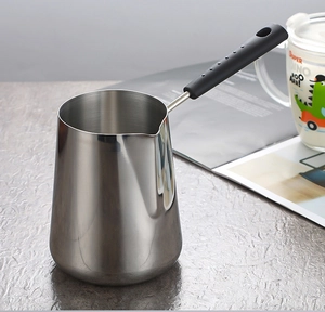 Detail of a mini stainless steel milk pot with a black handle on a textured tabletop