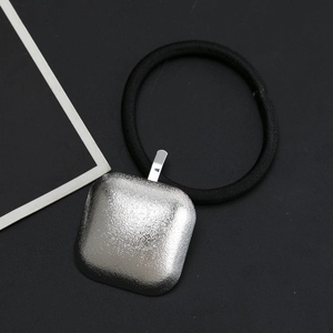 Detailed macro view of black elastic hair tie with textured silver square metal charm