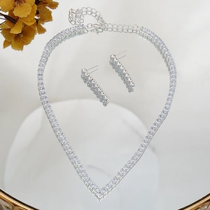 Macro shot of silver V-shaped necklace and zircon earrings set on a reflective surface