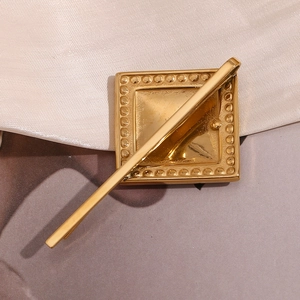 Détail d'une pince à cheveux carrée dorée avec strass sur fond de tissu satiné blanc
