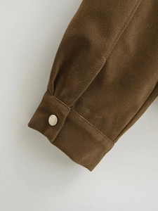 Detailaufnahme der kaffeebraunen Wildlederjacke mit einem silbernen Metalldruckknopf