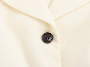 Close-up of tortoise shell button on cream elegant short blazer with textured fabric