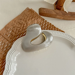 Detail of grey acetate hair claw clip on white ceramic plate with golden metal teeth