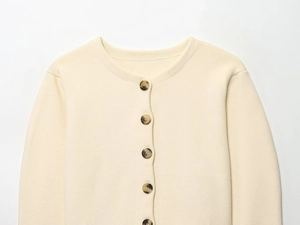 Detail of cream knit cardigan featuring a round neck and amber textured buttons
