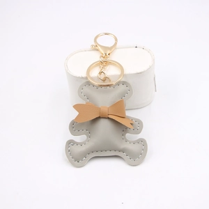 Detailed close-up of a grey leather bear keychain with a brown bow and gold metal clasp