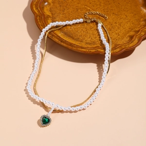 Detail of double-layer necklace with pearls, gold snake chain and green heart pendant