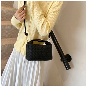 Detail of black woven shoulder bag with gold hardware worn by a model on stairs