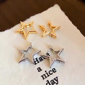 Star shaped gold and silver cutout earrings set on white paper and wood background