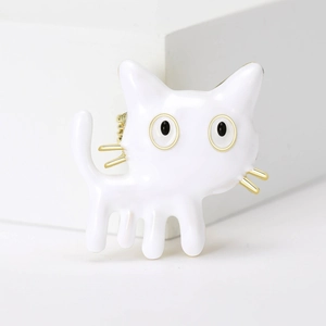 Detailed close-up of a cute white enamel cat brooch with gold metal whiskers on white cubes