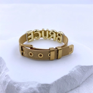 Detail of a gold mesh bracelet with BRUCE lettering on a white textured stone base