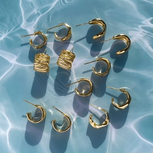 Flat lay of gold geometric titanium earrings on blue water ripple background