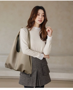 Close-up of beige lychee grain leather tote bag worn by model in a soft indoor setting