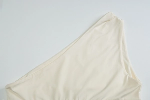 Detail of off-white one-shoulder knit top showing fine fabric texture and sleek neckline
