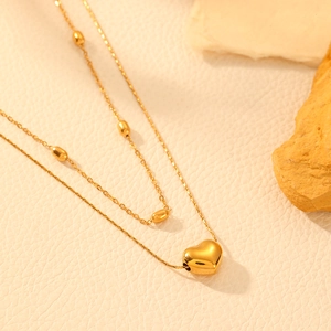 Close-up of golden double-layer necklace with heart pendant and beads on a textured stone